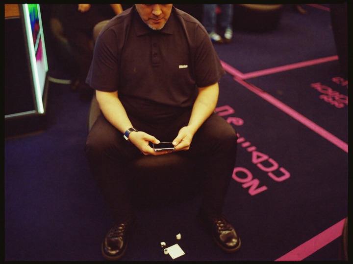 A man seated in a casino anteroom, phone held low in both hands