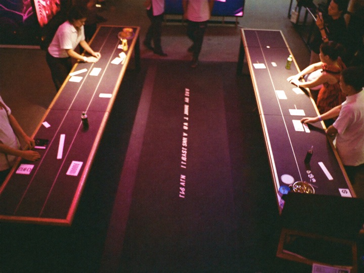 A pit seen from above, four tables in a row with dealers standing and guests seated