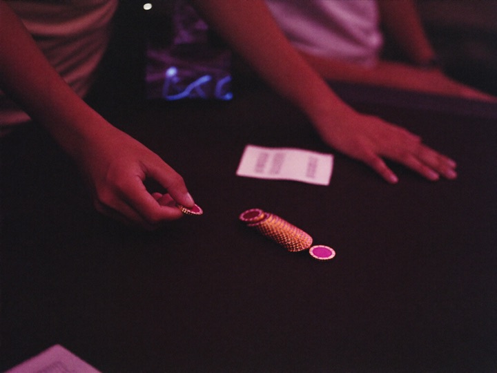 A dealer sliding a small stack of gold chips across dark felt toward a guest's hand