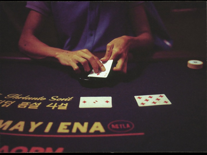 A dealer's hands drawing a card from an eight deck shoe on dark felt