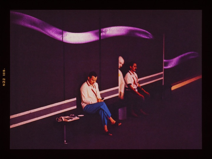 A man sitting alone on a bench in a hotel corridor, phone face down beside him