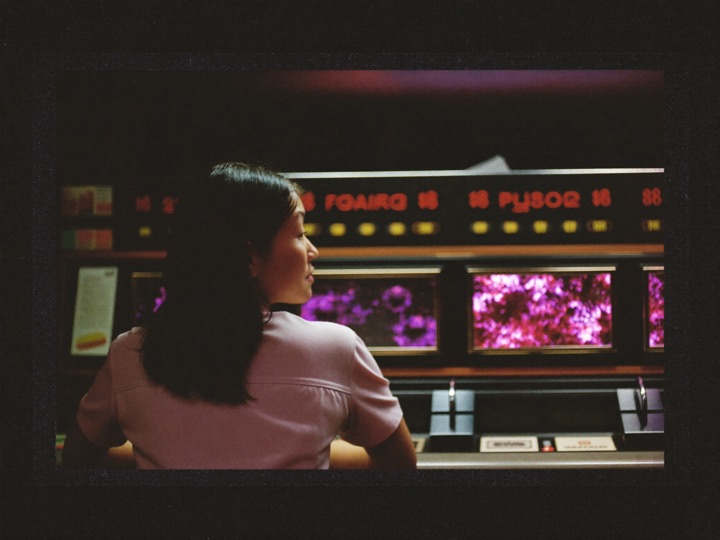 A woman seated at a bank of slot cabinets, seen from behind, the screen glow on her hair